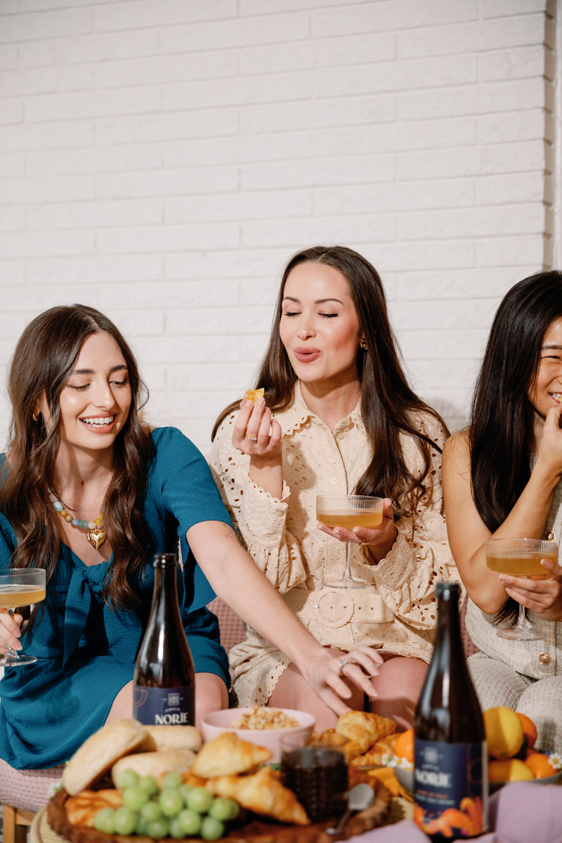 People holding glasses with Norïe Heart of Gold non-alcoholic sparkling drink nearby